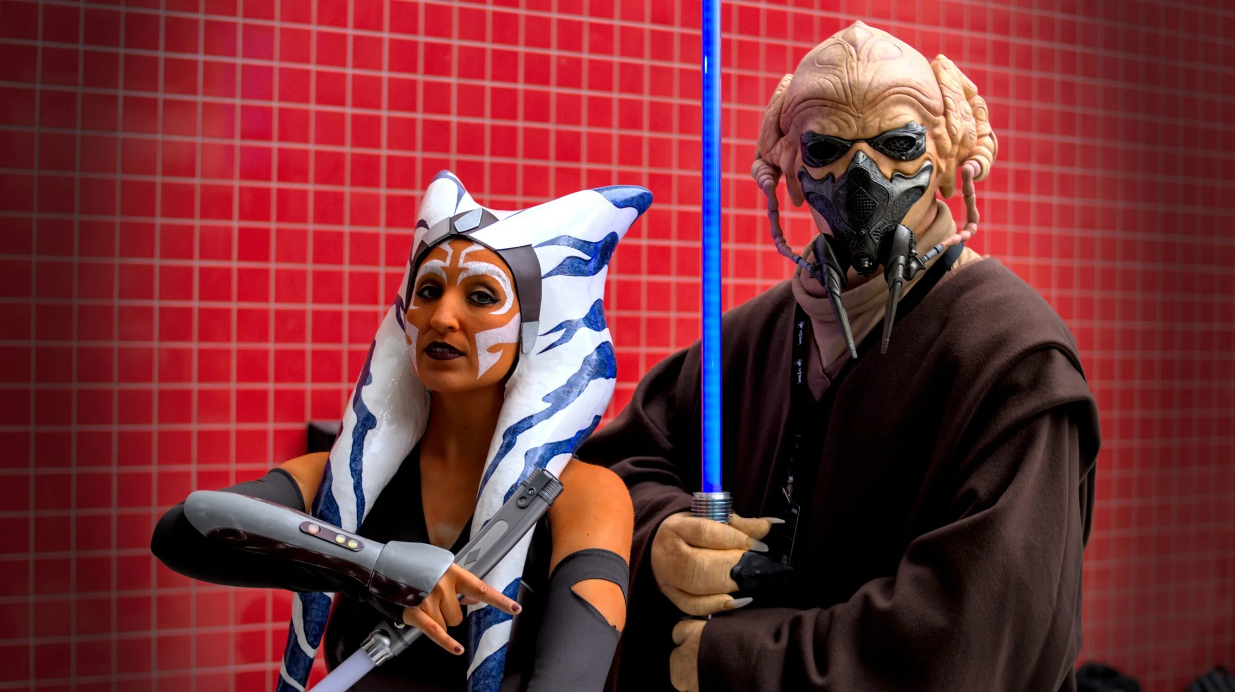 Pareja de personajes cosplay posando ante un fondo rojo