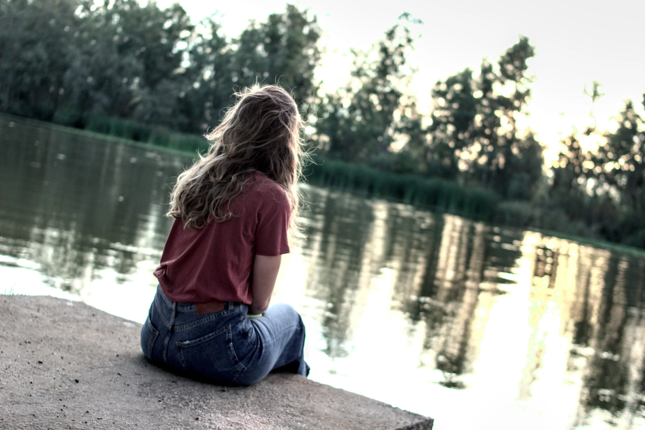 Retrato ambiental de una joven sentada junto al agua al atardecer